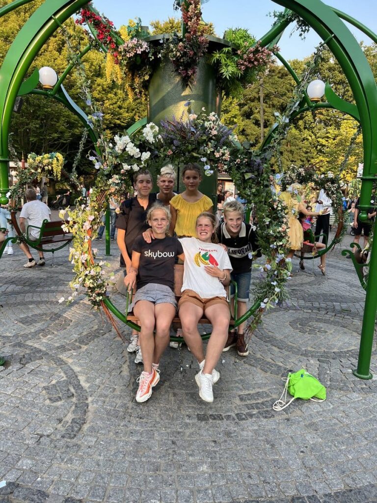 Zes kinderen bij een schommel versierd met bloemen en planten